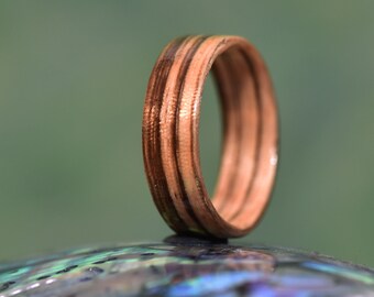 Op de afbeelding: Een houten ring met een bruin en wit gestreept patroon. De ring is gemaakt van meerdere lagen hout, waardoor een unieke en textuurrijke uitstraling ontstaat.