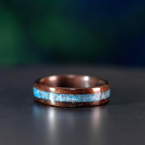 May include: A wooden ring with a band of light blue stone inlay. The ring is made of dark brown wood and has a smooth, polished finish. The stone inlay is a bright, contrasting color against the wood.