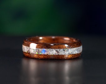 May include: A wooden ring with a thin band of iridescent opal inlay. The ring is brown with a polished finish.