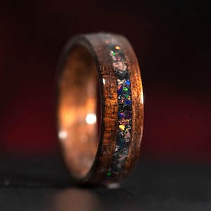 Może przedstawiać: Drewniany pierścień z oprawą z opalizującego opalu. Pierścień jest brązowy z ciemnobrązowym paskiem.
