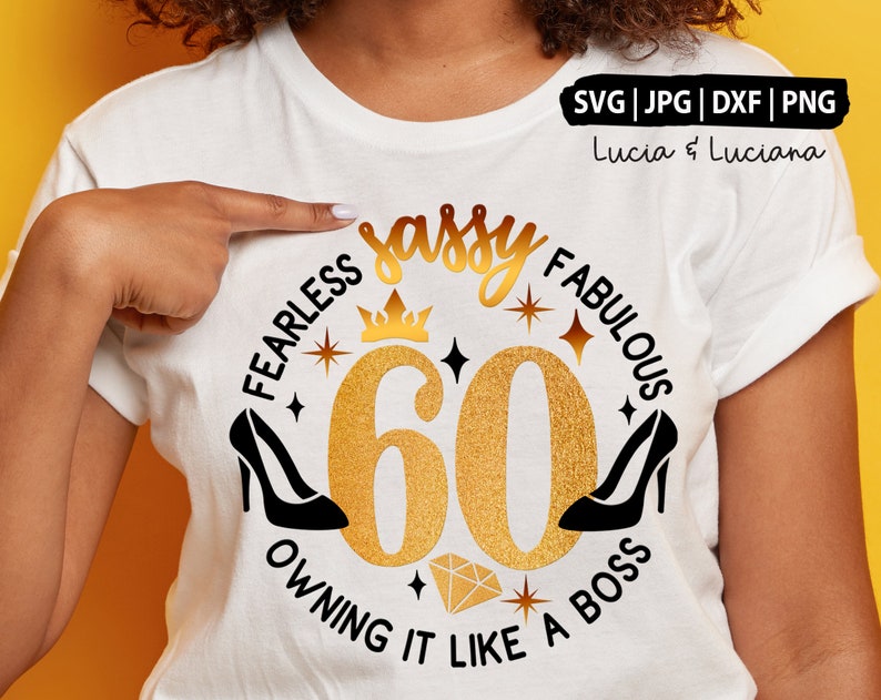 Op de afbeelding: Een wit T-shirt met een gouden glitterontwerp met de tekst "Fearless Sassy Fabulous 60 Owning It Like A Boss". Het ontwerp bevat een kroon, sterren en twee zwarte hakken.