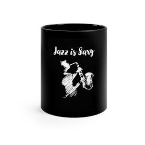 Puede incluir: Taza de cerámica negra con un diseño blanco de un saxofonista y el texto "Jazz is Saxxy".