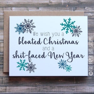 May include: A white card with a humorous Christmas greeting that reads "We wish you a bloated Christmas and a shit-faced New Year". The card is decorated with teal and black snowflakes.