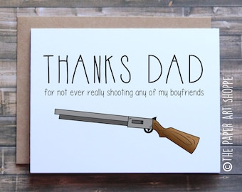 Może przedstawiać: Biała kartka z czarnym tekstem, który brzmi "THANKS DAD for not ever really shooting any of my boyfriends". Pod tekstem znajduje się kreskówkowy rysunek strzelby. Kartka leży na brązowej drewnianej powierzchni.