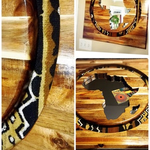 May include: A wooden table top with a circular inlay of an African continent shape. The inlay is surrounded by a black and gold patterned border. The table top is made of wood planks.