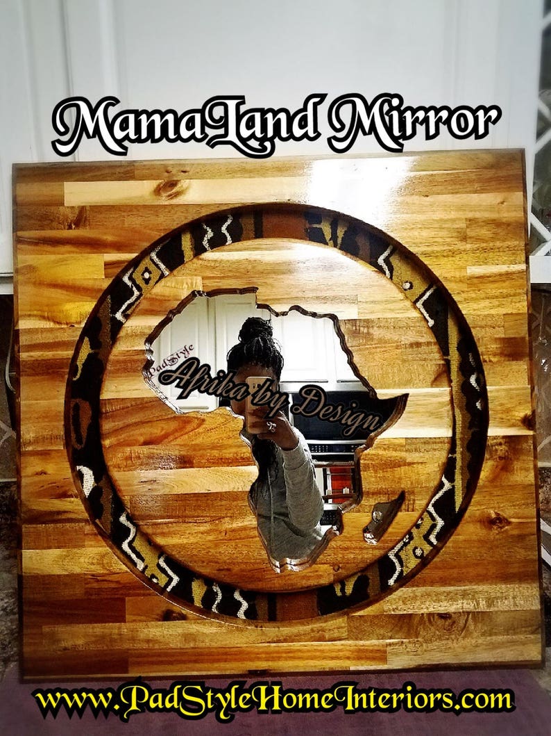 May include: A wooden framed mirror with a circular cutout in the shape of the continent of Africa. The cutout is surrounded by a patterned fabric border. The mirror is labeled "Mama Land Mirror" and "Africa by Design".