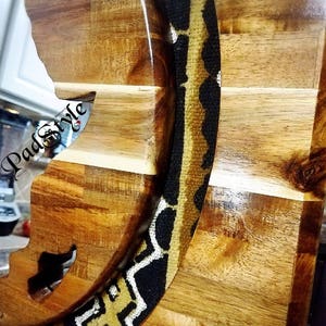 May include: A wooden cutting board with a carved out shape of a face. The board is decorated with a black and gold patterned fabric.