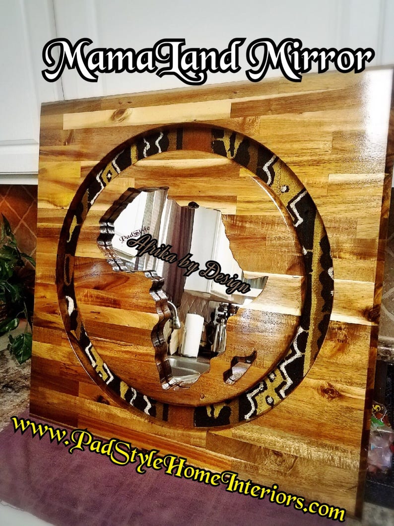 May include: A wooden wall mirror with a circular cutout in the shape of the continent of Africa. The cutout is filled with a patterned fabric in shades of brown, gold, and black. The mirror is labeled "Africa by Design" and "Mama Land Mirror".
