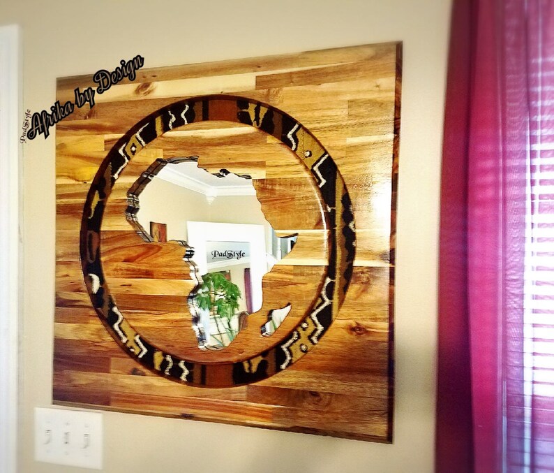 May include: A wooden wall art piece featuring a circular cutout of the continent of Africa with a patterned border. The wood is a light brown color and the pattern is a mix of black, white, and brown.