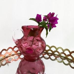 May include: A pink glass pitcher with a clear handle and a textured bubble design. The pitcher is filled with pink flowers.