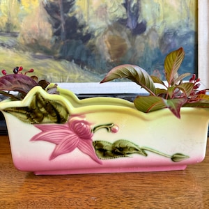 May include: A vintage ceramic planter with a pink and green glaze. The planter features a raised floral design and is perfect for displaying small plants or flowers.
