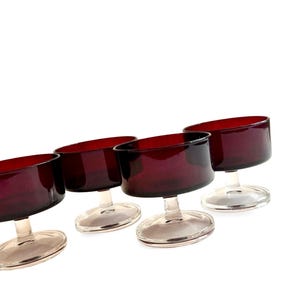 May include: Four vintage stemmed dessert glasses. The bowls are a deep burgundy color, and the stems and bases are clear. The glasses are arranged at a slight angle against a white background.