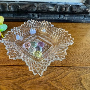 May include: A clear glass dish with a diamond pattern and a square center. The dish is filled with small, colorful glass marbles.