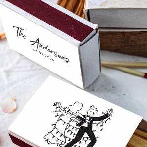 Könnte beinhalten: Streichholzschachteln mit bordeauxrotem und weißem Design. Eine Schachtel trägt den Text "The Andersons 01.01.2024". Eine weitere Schachtel zeigt eine Schwarz-Weiß-Illustration eines tanzenden Paares mit Lichtern. Die Streichhölzer haben rote Spitzen.