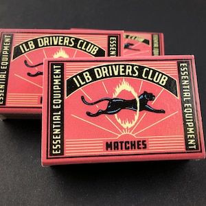 May include: Two rectangular matchboxes with a red background and black borders. The design features a black panther jumping through a yellow ring of fire, with the text ILB DRIVERS CLUB and ESSENTIAL EQUIPMENT MATCHES printed in black and yellow.