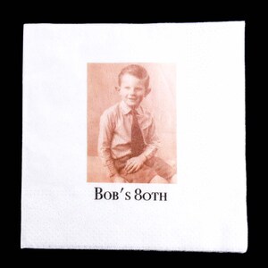 K&ouml;nnte beinhalten: Wei&szlig;e Papierserviette mit einem Sepia-Ton-Bild eines jungen Jungen in Hemd und Krawatte. Der Text "Bob's 80TH" ist darunter gedruckt, was auf eine Geburtstagsfeier hindeutet.