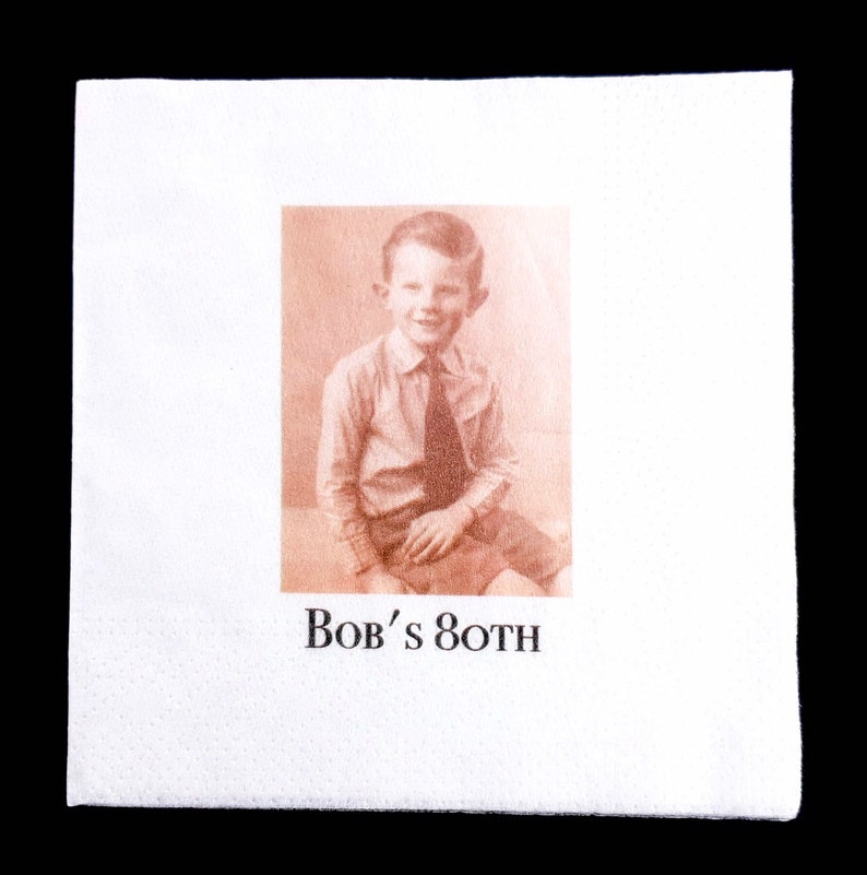 K&ouml;nnte beinhalten: Wei&szlig;e Papierserviette mit einem Sepia-Ton-Bild eines jungen Jungen in Hemd und Krawatte. Der Text "Bob's 80TH" ist darunter gedruckt, was auf eine Geburtstagsfeier hindeutet.