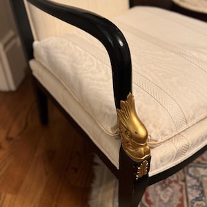 Puede incluir: Sill&oacute;n antiguo con estructura negra y detalles dorados. Los reposabrazos son curvos, y el asiento y el respaldo est&aacute;n tapizados en tela crema con un patr&oacute;n de rayas. Las patas de la silla son oscuras, y los detalles dorados a&ntilde;aden elegancia.