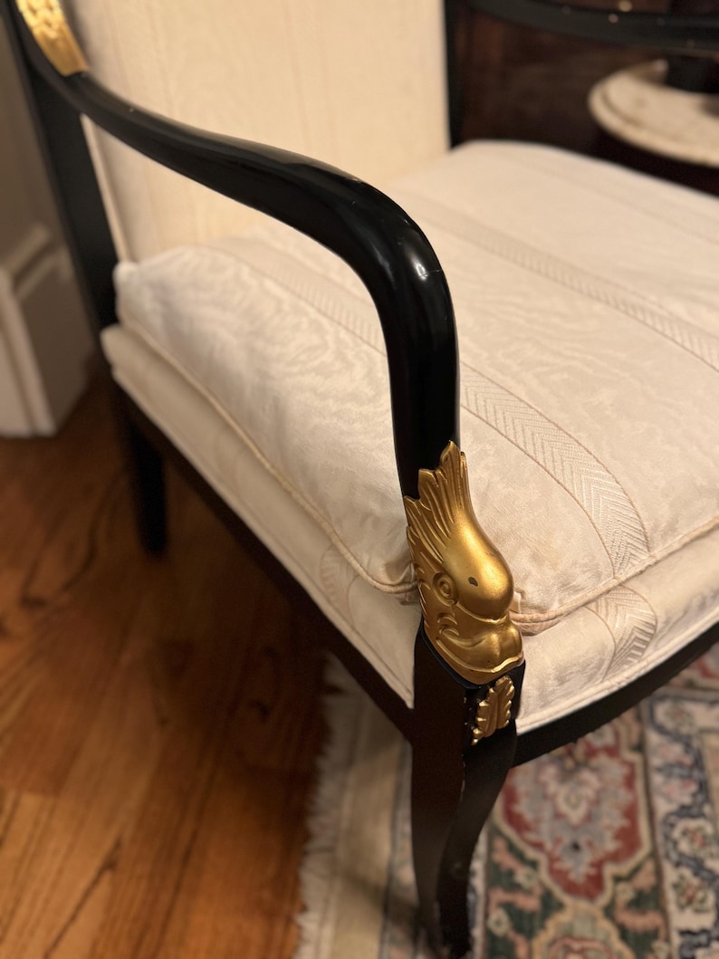 Puede incluir: Sill&oacute;n antiguo con estructura negra y detalles dorados. Los reposabrazos son curvos, y el asiento y el respaldo est&aacute;n tapizados en tela crema con un patr&oacute;n de rayas. Las patas de la silla son oscuras, y los detalles dorados a&ntilde;aden elegancia.