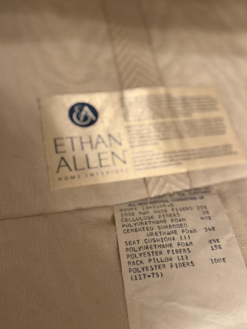 Puede incluir: Primer plano de una etiqueta de Ethan Allen Home Interiors. La etiqueta enumera los materiales utilizados en el producto, incluyendo fibras artificiales, fibras de celulosa, espuma de poliuretano y fibras de poli&eacute;ster.