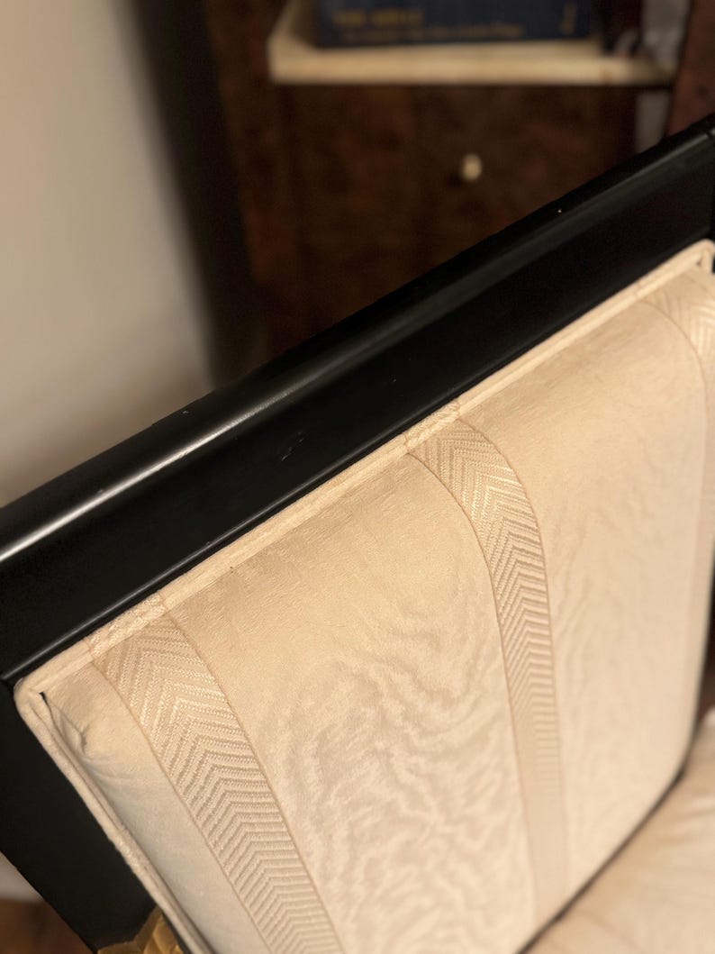 Puede incluir: Primer plano de un marco de silla de madera negra con un respaldo tapizado de color crema. El respaldo presenta paneles verticales con un sutil patr&oacute;n de espiga, creando un dise&ntilde;o texturizado. La silla parece ser parte de un conjunto.