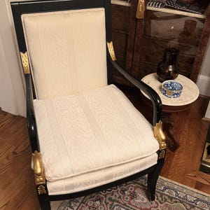 Puede incluir: Un elegante sill&oacute;n negro con asiento y respaldo crema estampados. La silla presenta detalles dorados en los brazos y las patas, a&ntilde;adiendo un toque de lujo. Un mueble cl&aacute;sico.