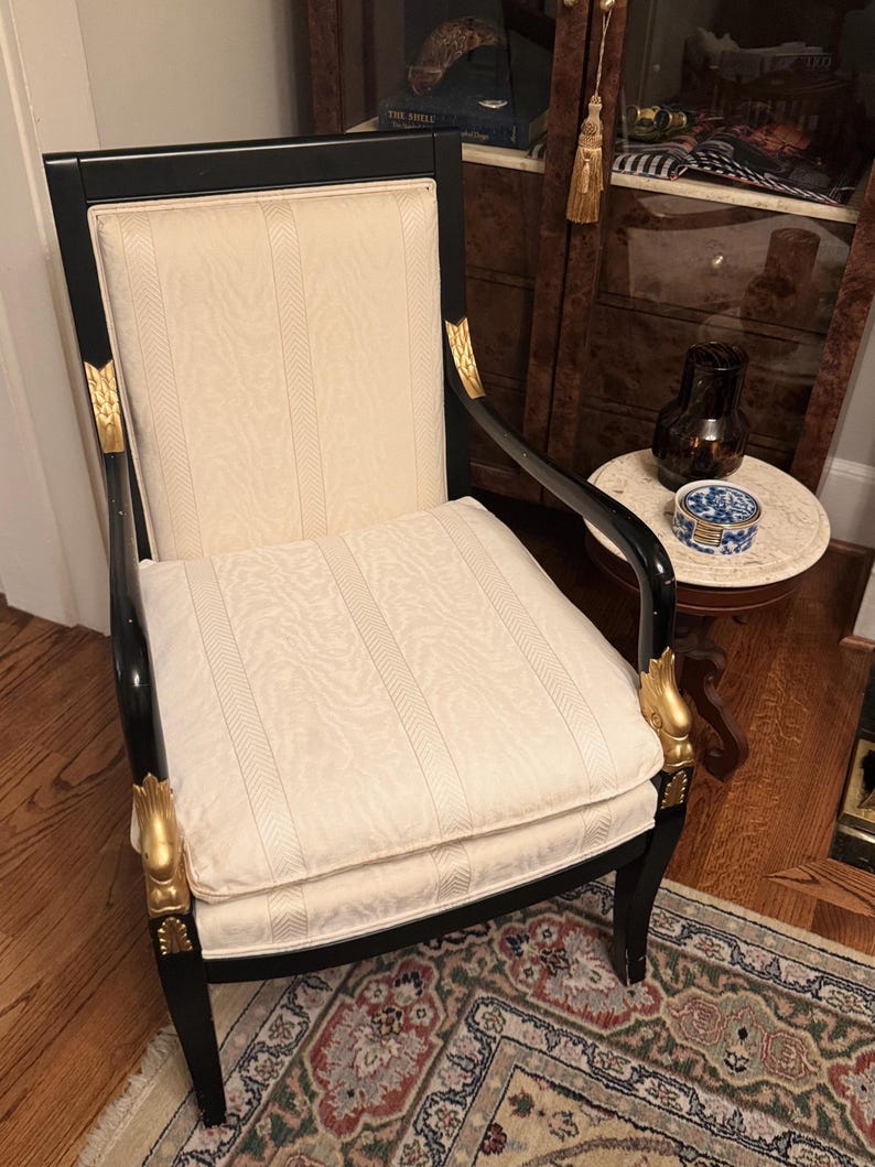 Puede incluir: Un elegante sill&oacute;n negro con asiento y respaldo crema estampados. La silla presenta detalles dorados en los brazos y las patas, a&ntilde;adiendo un toque de lujo. Un mueble cl&aacute;sico.