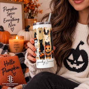 Może przedstawiać: Biały cylindryczny kubek ze słomką metalową z grafiką o tematyce Halloween. Wzór przedstawia ducha w kapeluszu czarownicy, czarnego kota, dynię, nietoperze oraz pajęczynę wraz z napisem Spooky Season umieszczonym na powierzchni naczynia.