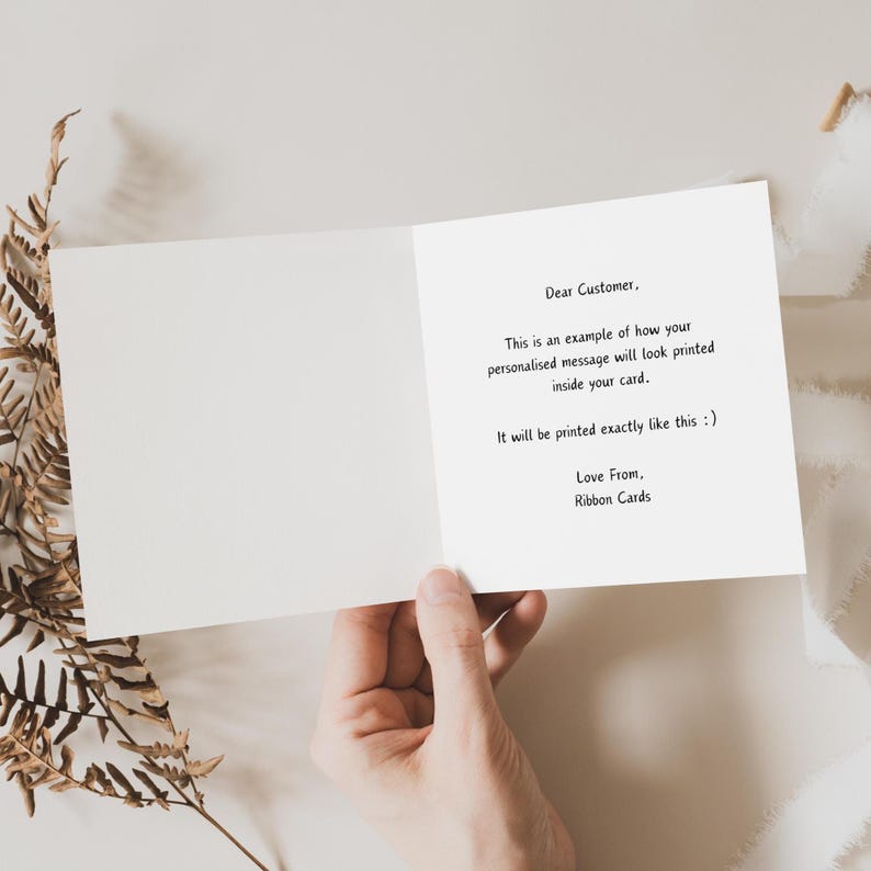 May include: A white card with a message explaining how personalized messages will be printed on the inside of the card. The message reads: "Dear Customer, This is an example of how your personalized message will look printed inside your card. It will be printed exactly like this :) Love From, Ribbon Cards."
