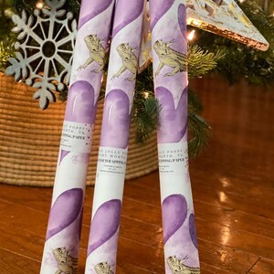 May include: Three rolls of purple and white wrapping paper with a watercolor design of hearts and a lizard. The paper is labeled "The Jolly Poppy Fort Worth, TX Gift Wrapping".