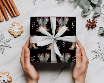 May include: A wrapped gift with a black background featuring a repeating pattern of cowboy boots and string lights. The gift is tied with a silver ribbon. The background includes holiday decorations like snowflakes and cookies.