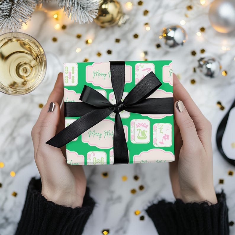 以下が含まれることがあります： 緑色の包装紙で包まれたギフト。トランプのマークと「Merry Mardi」の文字が繰り返されるパターン。大きな黒いサテンのリボンで結ばれています。背景には休日の装飾が含まれています。