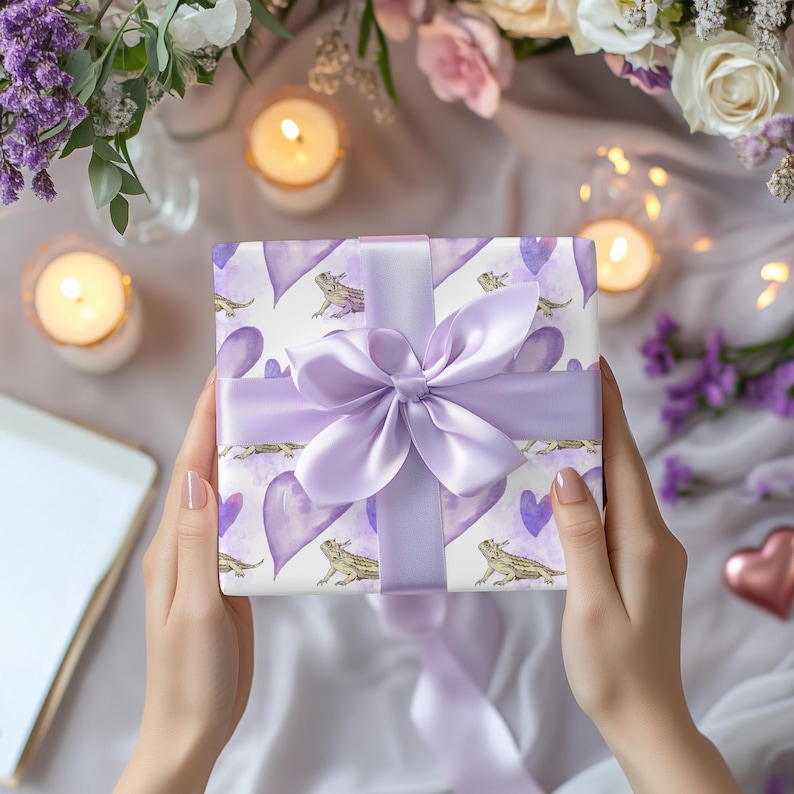 May include: A purple gift box with a white background and a purple ribbon. The box is decorated with a pattern of purple hearts and small lizards.
