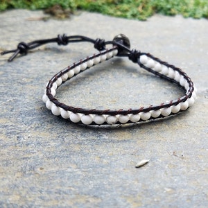 May include: A brown leather bracelet with white beads. The bracelet has a simple adjustable closure.