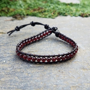 May include: A brown leather bracelet with a double row of dark red gemstone beads.