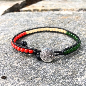 May include: A leather bracelet with red, white, and green beads and a silver tree of life charm.