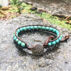 May include: A turquoise beaded bracelet with a brown leather wrap and a silver tree of life charm.