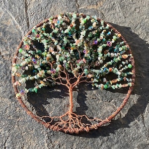 May include: A copper wire tree of life sculpture with green and brown gemstone leaves. The tree is surrounded by a copper wire circle.