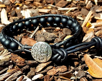 Può includere: Braccialetto in pelle nera con perline di onice nero e un bottone d'argento a forma di albero della vita.