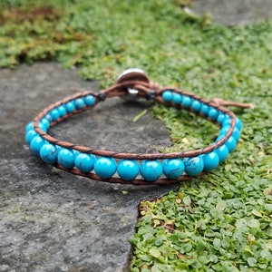 May include: A turquoise beaded bracelet with a brown leather cord. The bracelet has a silver clasp.