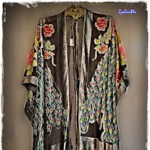 Puede incluir: Kimono de terciopelo gris con dise&ntilde;o de plumas de pavo real en tonos verdes, amarillos y rojos. El kimono tiene detalles florales y flecos de cuentas. El texto "2za2uuBlu" es visible en la esquina superior derecha.