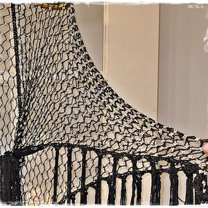 May include: Black and silver crocheted shawl with a net-like design. The shawl features a fringe along the bottom edge and is embellished with silver accents. The top edge has a decorative beaded trim.