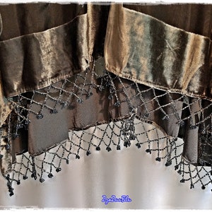 Puede incluir: Primer plano de un textil decorativo con un dise&ntilde;o en capas. El textil presenta secciones de terciopelo marr&oacute;n y una tela transparente y oscura. El borde inferior est&aacute; adornado con una franja de cuentas. El textil tiene un dise&ntilde;o de pluma de pavo real.