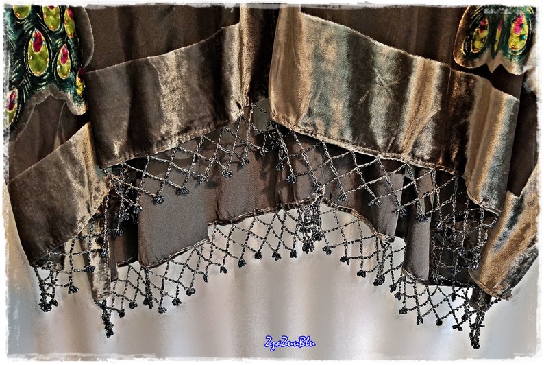 Puede incluir: Primer plano de un textil decorativo con un dise&ntilde;o en capas. El textil presenta secciones de terciopelo marr&oacute;n y una tela transparente y oscura. El borde inferior est&aacute; adornado con una franja de cuentas. El textil tiene un dise&ntilde;o de pluma de pavo real.