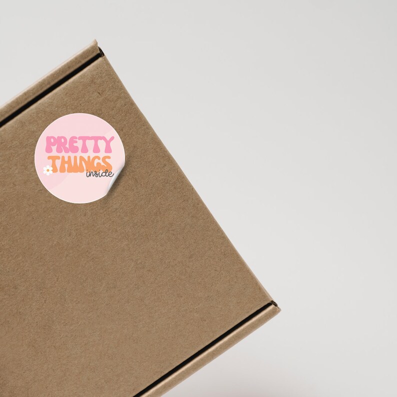 Puede incluir: Una caja de cart&oacute;n marr&oacute;n con una pegatina rosa y naranja que dice "Pretty Things Inside".