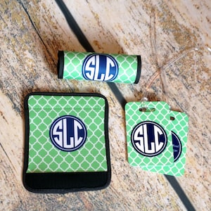 May include: Set of three green and white luggage tags with a navy blue monogram "SLC" in a circle. The tags are attached to a clear luggage strap. There is also a green and white luggage handle wrap with the same monogram.