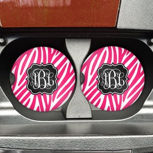 May include: Two pink and white zebra print car coasters with black monogram initials "B.B.L." in the center of each coaster.