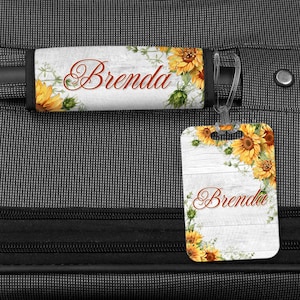 May include: A luggage handle wrap and luggage tag featuring a sunflower design with the name "Brenda" in a decorative script. The background is a white wood grain pattern. The sunflowers are yellow and orange.