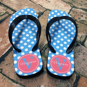 May include: A pair of blue flip flops with white polka dots and a pink circle with the letter "V" and the word "Virginia" printed on each.
