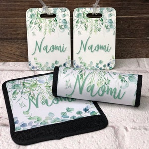 May include: Set of three luggage tags and a luggage strap featuring a watercolor design of green leaves and the name "Naomi" printed in green.